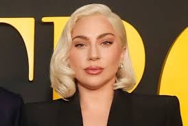 Woman with platinum blonde bob hairstyle and red lipstick wearing black jacket at event