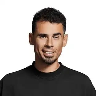 Headshot of a smiling man with dark hair and facial hair wearing a black t-shirt against a white background