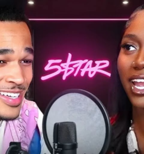 Two people smiling at microphone in studio with pink STAR neon sign glowing in background