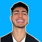 Portrait of a young man with dark hair and beard, smiling at the camera, wearing a black shirt against a bright blue background