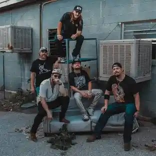 Five band members posing together outside, with one standing on a box behind the others in a playful group shot