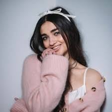 Young woman with dark hair wearing a white headband and pink ribbed sweater, smiling at the camera