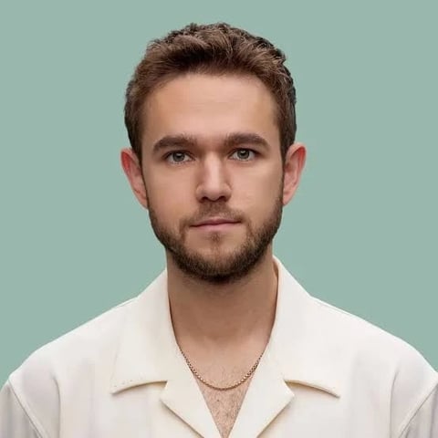 Portrait of a man with brown hair and facial hair wearing a cream-colored shirt against a mint green background