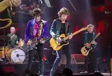 Rock band performing on stage with musicians playing drums, bass, and guitars under stage lighting