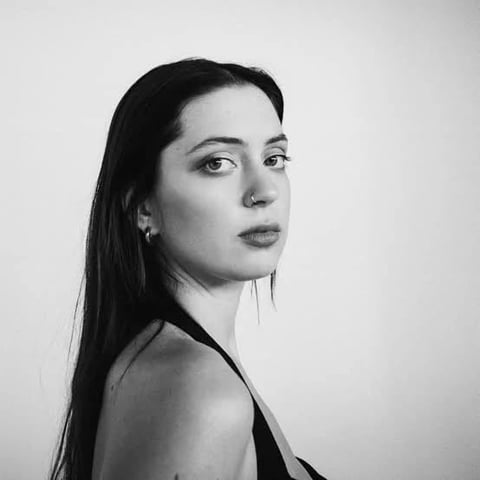 Black and white portrait of a woman with long dark hair looking over her shoulder at the camera against a plain background
