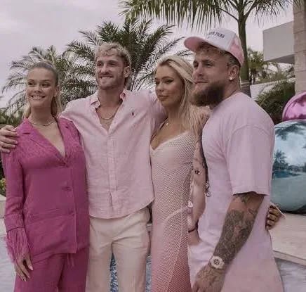 Four people dressed in pink outfits posing together outdoors with palm trees in the background