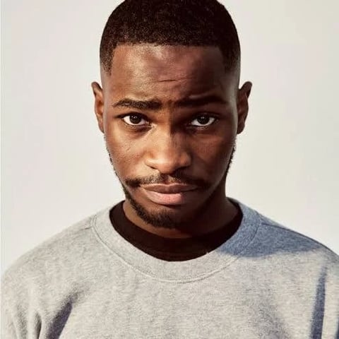 Headshot of a man with short dark hair and a beard wearing a light gray t-shirt against a neutral background