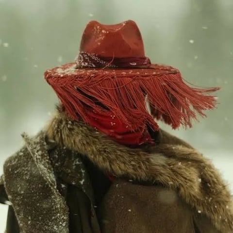 Meerkat wearing a red fringed cowboy hat and brown fur coat in falling snow