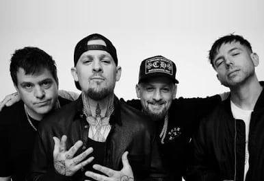 Four men in black and white portrait pose together, one wearing a cap, against a light background